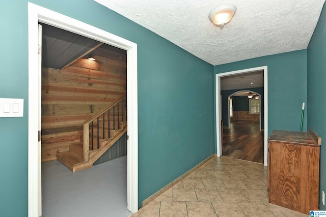 corridor featuring wood walls, a textured ceiling, and light tile patterned floors