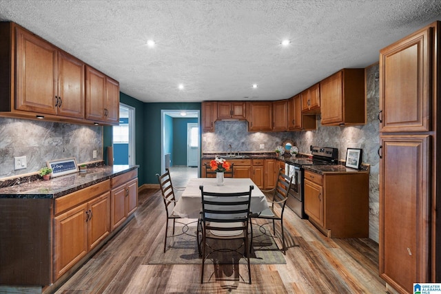 kitchen featuring sink, backsplash, a kitchen bar, stainless steel electric range oven, and hardwood / wood-style floors