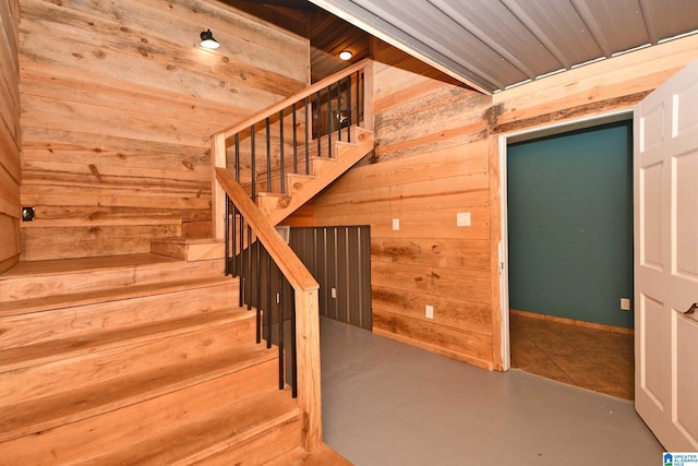 stairway with wood walls, concrete floors, and wooden ceiling