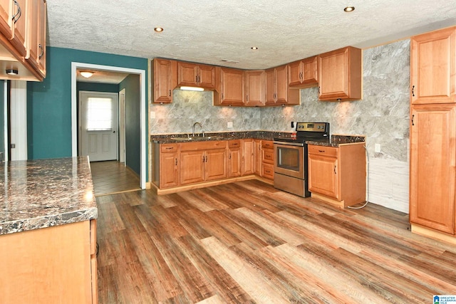 kitchen with sink, electric range, a textured ceiling, wood-type flooring, and dark stone counters