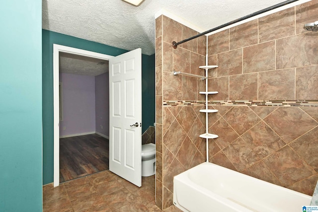 bathroom featuring toilet, tile patterned floors, tile walls, a textured ceiling, and tiled shower / bath