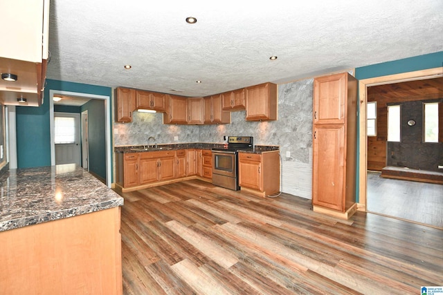 kitchen with sink, light wood-type flooring, a textured ceiling, dark stone counters, and stainless steel electric stove