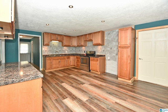 kitchen featuring sink, dark stone counters, light hardwood / wood-style flooring, and stainless steel range with electric cooktop