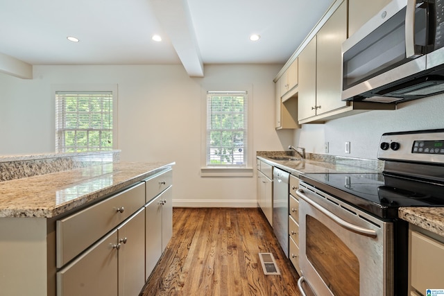 kitchen with appliances with stainless steel finishes, sink, light stone counters, cream cabinets, and hardwood / wood-style flooring