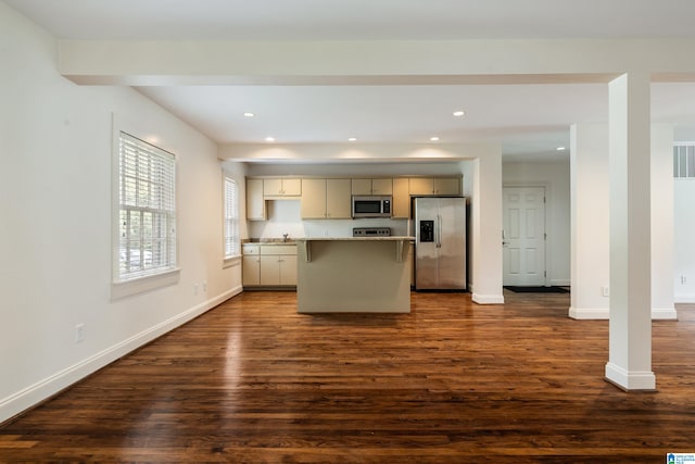 kitchen featuring stainless steel appliances, light stone counters, cream cabinets, a kitchen island, and dark wood-type flooring