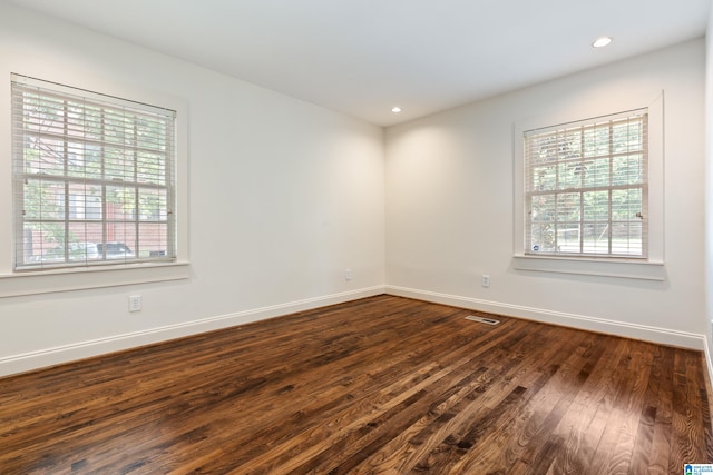 empty room with a wealth of natural light and dark hardwood / wood-style floors