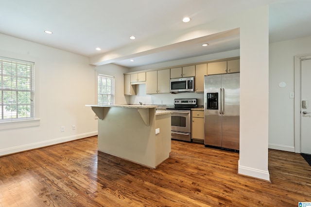 kitchen featuring a kitchen breakfast bar, dark wood-type flooring, cream cabinets, light stone countertops, and stainless steel appliances