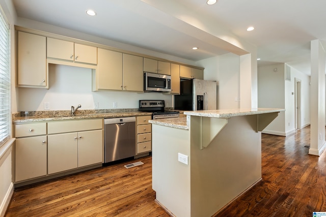 kitchen with appliances with stainless steel finishes, a center island, cream cabinetry, and dark hardwood / wood-style floors