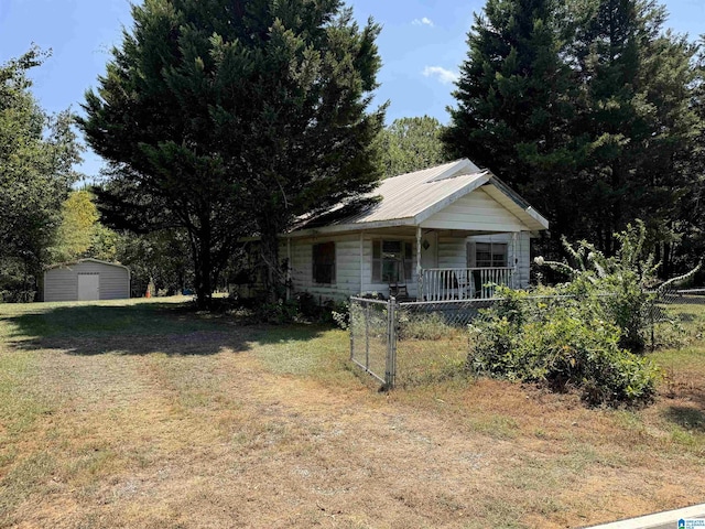 view of front facade featuring metal roof, covered porch, fence, an outdoor structure, and a front lawn