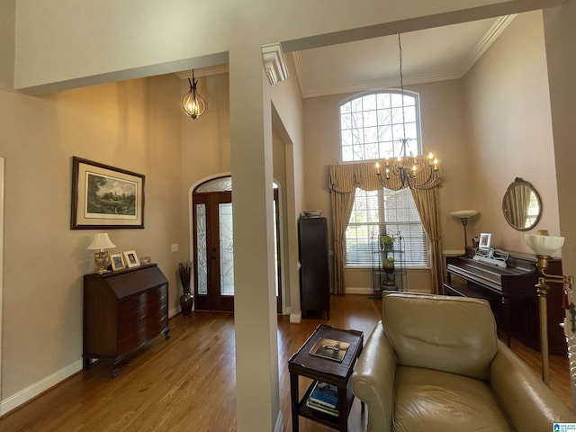 interior space with crown molding, a towering ceiling, wood finished floors, a chandelier, and baseboards