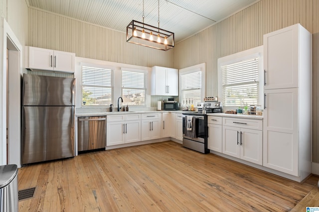 kitchen with decorative light fixtures, stainless steel appliances, white cabinetry, and light hardwood / wood-style flooring