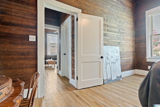 corridor with light wood-type flooring and wooden walls