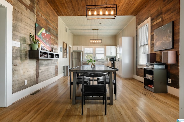 dining area featuring light wood-type flooring and wooden walls