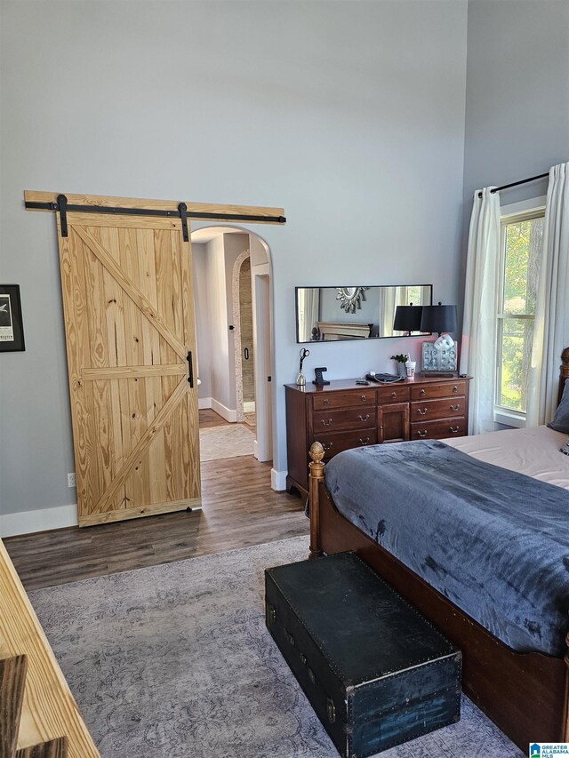 bedroom with hardwood / wood-style flooring, a high ceiling, and a barn door