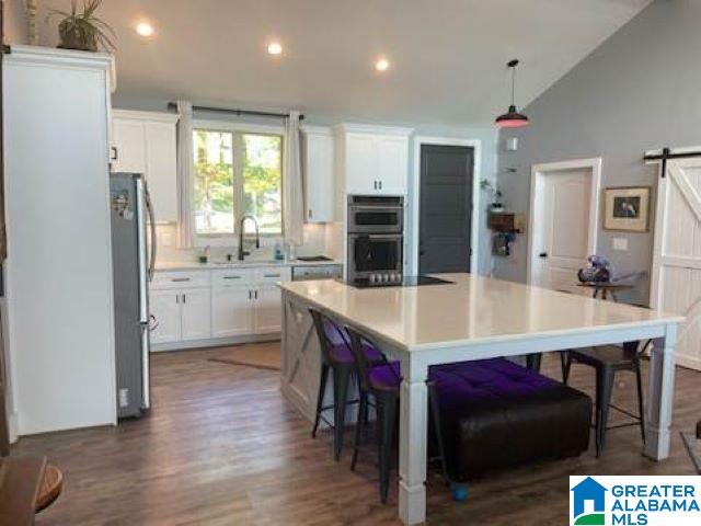 kitchen with white cabinets, a center island, stainless steel appliances, lofted ceiling, and dark hardwood / wood-style floors