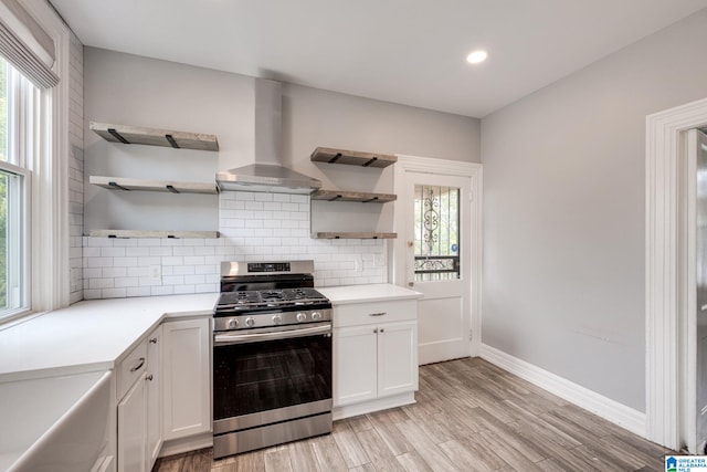 kitchen with light hardwood / wood-style floors, wall chimney exhaust hood, stainless steel gas range, and white cabinets