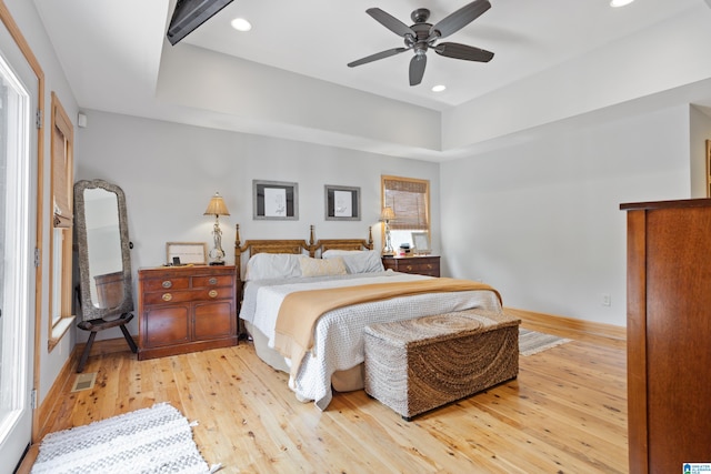 bedroom with ceiling fan, light hardwood / wood-style flooring, and a tray ceiling