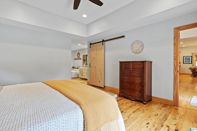 bedroom with light hardwood / wood-style floors, a barn door, ceiling fan, and ensuite bathroom