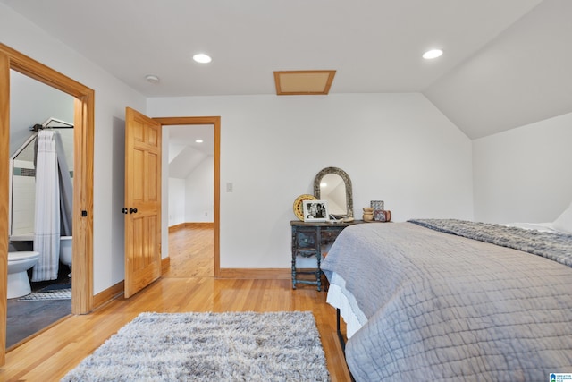 bedroom with vaulted ceiling, connected bathroom, and light hardwood / wood-style floors