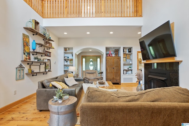 living room featuring light hardwood / wood-style flooring, built in features, and a towering ceiling