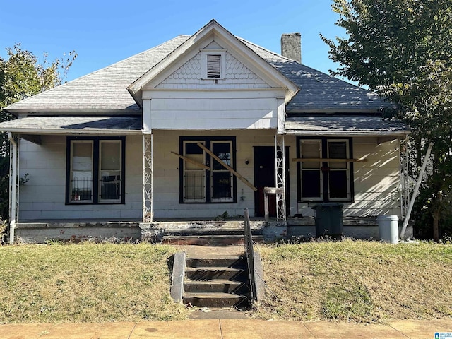 view of front facade featuring a porch, roof with shingles, and a chimney