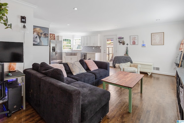 living room with dark wood-type flooring, beverage cooler, crown molding, and sink