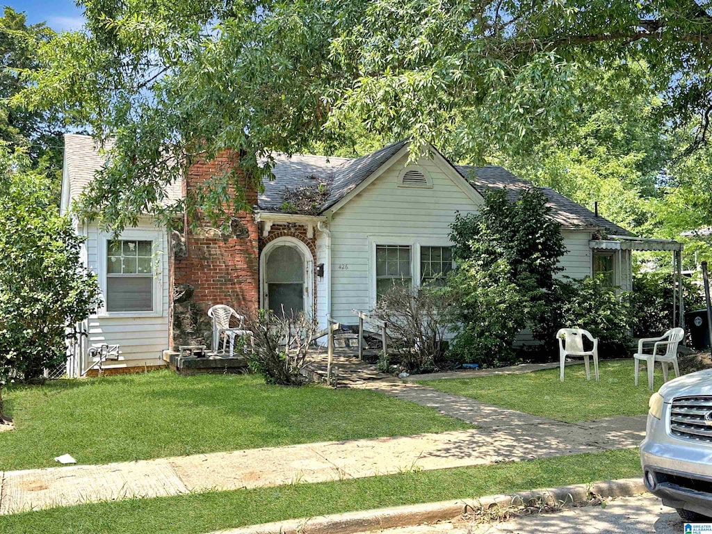 view of front of property with brick siding, a front lawn, and roof with shingles