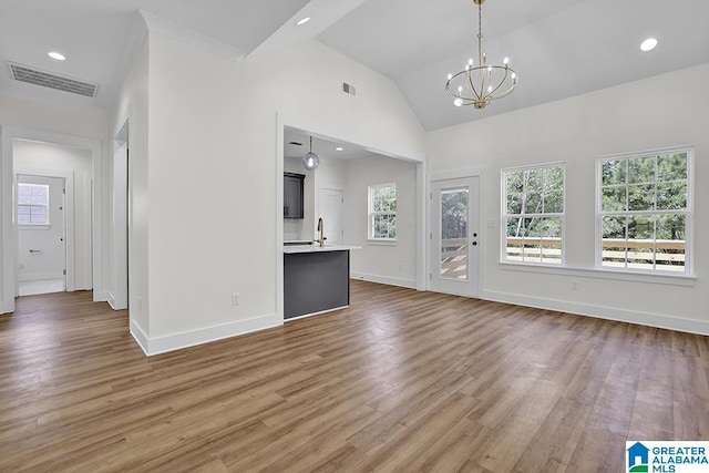 unfurnished living room with a chandelier, lofted ceiling, wood finished floors, visible vents, and baseboards