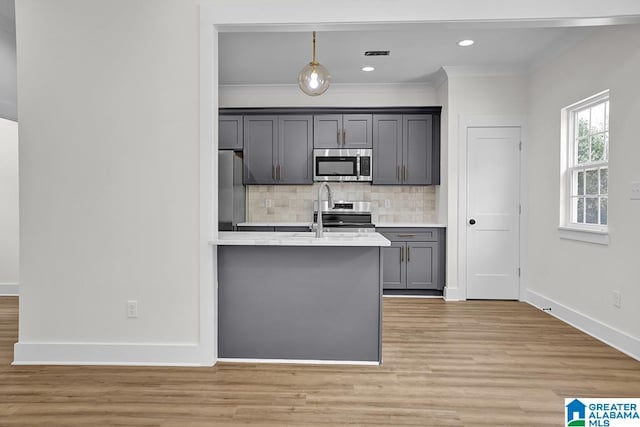 kitchen with light wood-type flooring, stainless steel appliances, tasteful backsplash, and decorative light fixtures