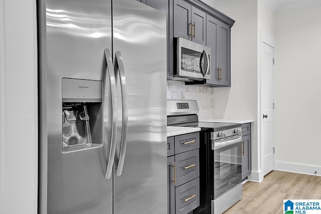 kitchen with appliances with stainless steel finishes, light hardwood / wood-style flooring, gray cabinets, and tasteful backsplash