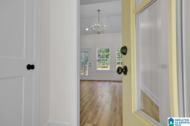 hallway with baseboards, light wood-style flooring, and a notable chandelier