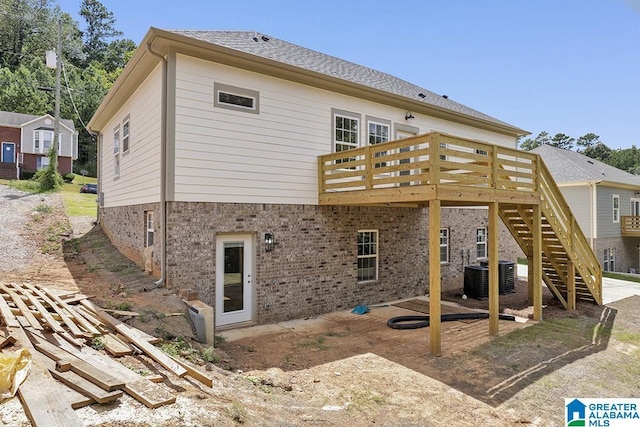 rear view of house with brick siding, central air condition unit, a shingled roof, stairway, and a deck