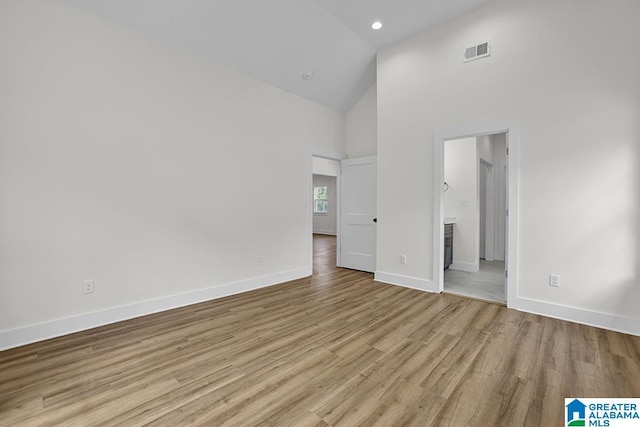 unfurnished bedroom with light wood finished floors, visible vents, ensuite bath, high vaulted ceiling, and baseboards