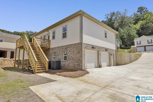 view of property exterior featuring a garage, brick siding, concrete driveway, stairway, and a wooden deck