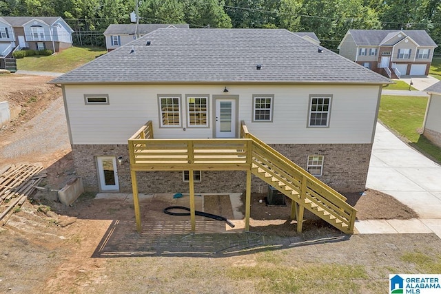 rear view of house featuring brick siding, roof with shingles, and stairs