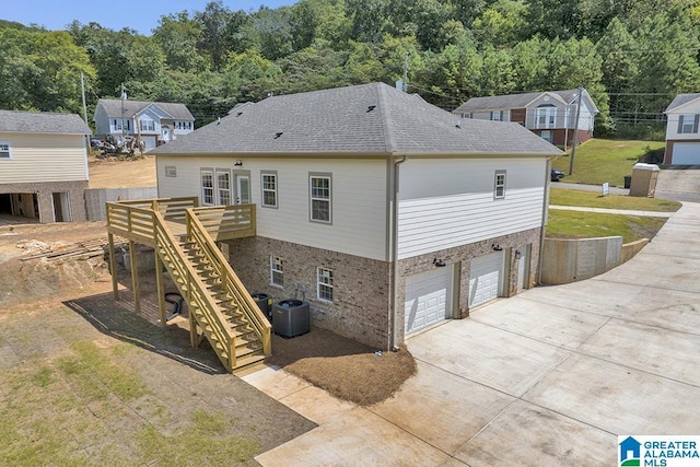 back of property with a deck, central AC unit, an attached garage, brick siding, and stairway