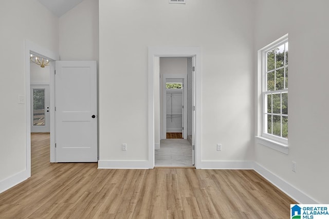 unfurnished bedroom featuring connected bathroom, a high ceiling, visible vents, baseboards, and light wood-type flooring