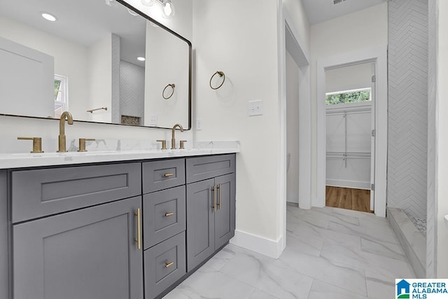 bathroom featuring marble finish floor, a sink, a spacious closet, and double vanity