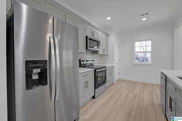 kitchen with appliances with stainless steel finishes, gray cabinetry, backsplash, ornamental molding, and light hardwood / wood-style flooring