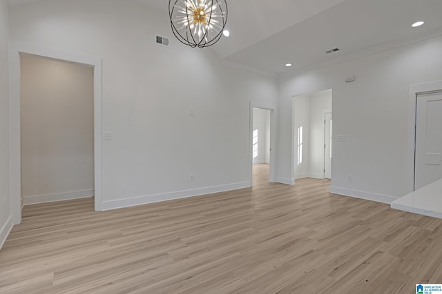 spare room featuring a notable chandelier, a towering ceiling, ornamental molding, and light hardwood / wood-style floors