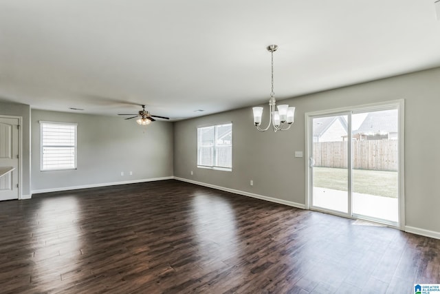 spare room featuring a wealth of natural light, ceiling fan with notable chandelier, and dark hardwood / wood-style flooring