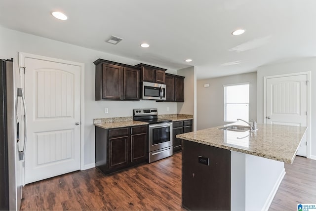 kitchen with stainless steel appliances, dark hardwood / wood-style floors, sink, light stone countertops, and a kitchen island with sink