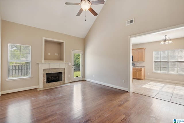 unfurnished living room featuring plenty of natural light, ceiling fan with notable chandelier, hardwood / wood-style floors, and a tile fireplace