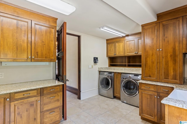 laundry room with washing machine and clothes dryer, light tile patterned floors, and cabinets