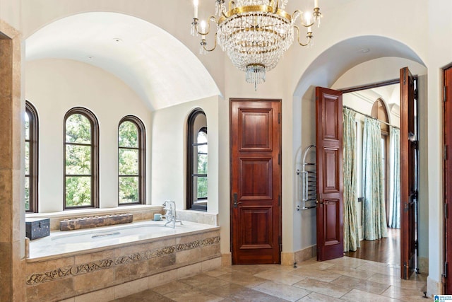 bathroom featuring tiled tub, a notable chandelier, and hardwood / wood-style floors