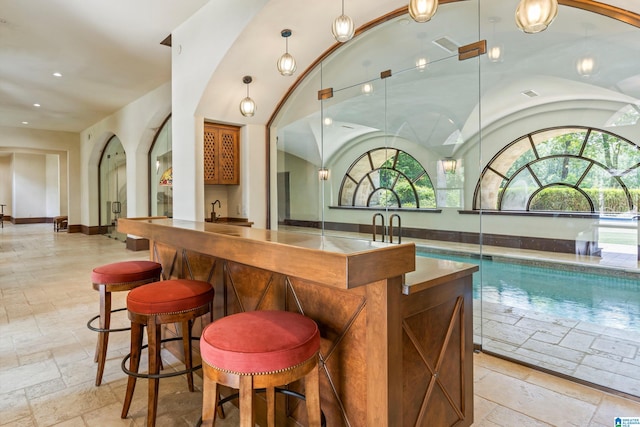 bar with sink, vaulted ceiling, hanging light fixtures, and light tile patterned flooring