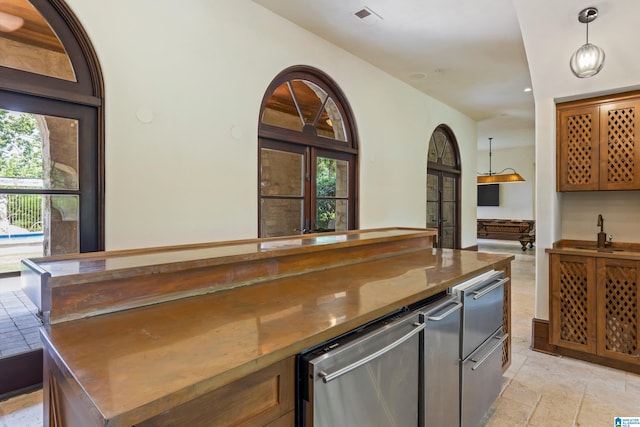 kitchen featuring stainless steel dishwasher, sink, light tile patterned floors, dark stone countertops, and hanging light fixtures