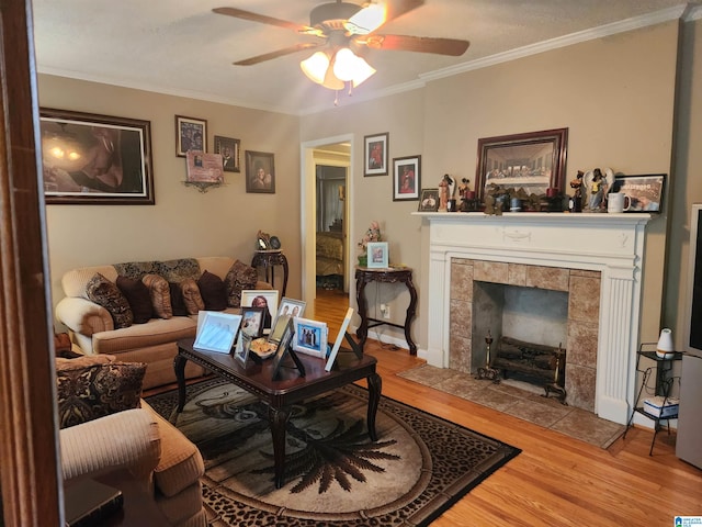 living room featuring ceiling fan, crown molding, light hardwood / wood-style flooring, and a tiled fireplace