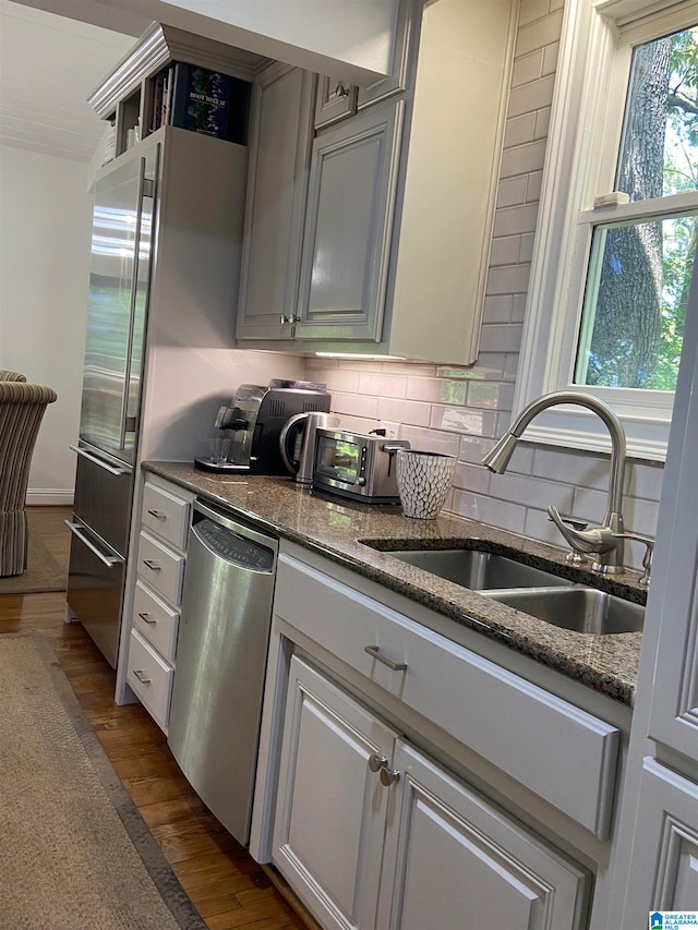 kitchen featuring dishwasher, dark wood-type flooring, dark stone countertops, and sink