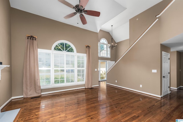 unfurnished living room with a towering ceiling, ceiling fan with notable chandelier, and dark wood-type flooring